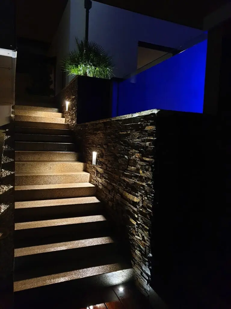 Escalier extérieur en bois illuminé, avec mur en pierre et piscine éclairée en bleu à Évian-Les-Bains en Haute-Savoie (74)