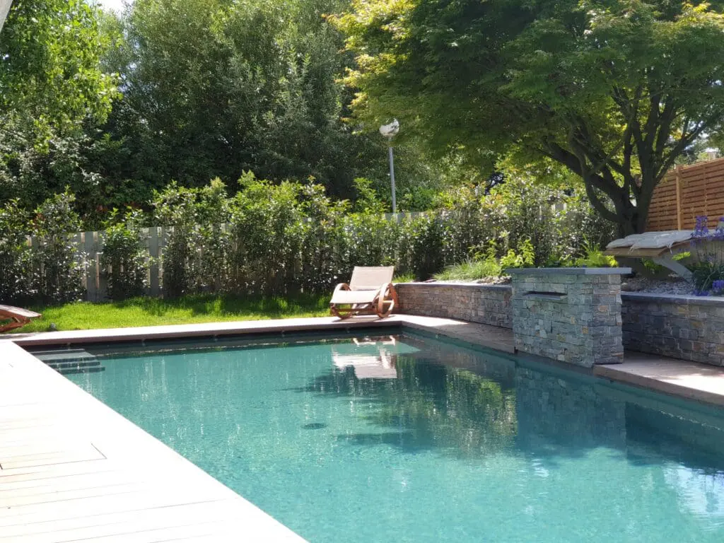 Piscine rectangulaire avec cascade en pierre naturelle, terrasse en bois et jardin paysager à Chens-sur-Léman en Haute-Savoie (74)