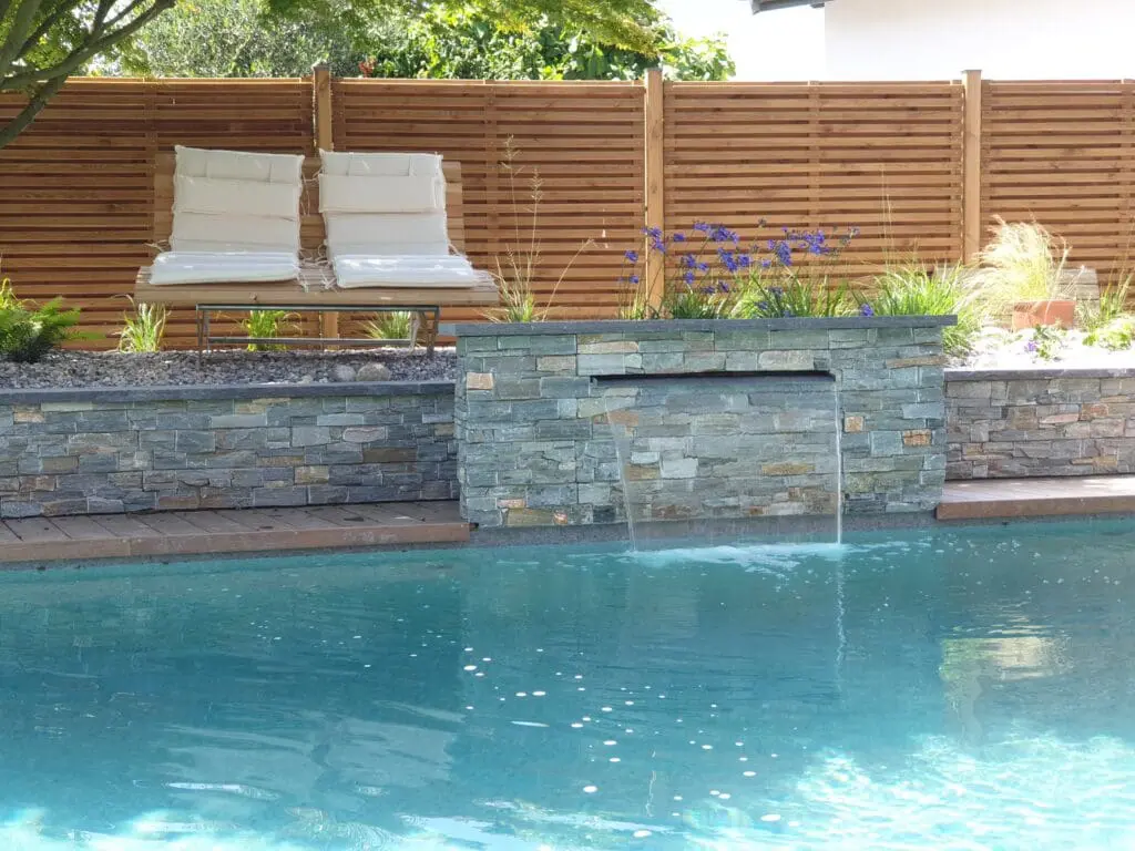 Piscine avec cascade en pierre naturelle, terrasse en bois et clôture en bois à Chens-sur-Léman en Haute-Savoie (74)