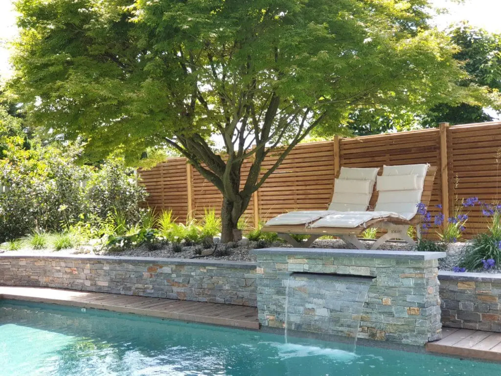 Piscine avec terrasse en bois, mur en pierre naturelle, cascade et érable japonais à Chens-sur-Léman en Haute-Savoie (74)