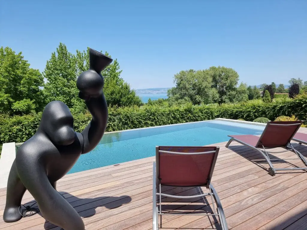 Piscine à débordement en béton brut avec plage en bois exotique et vue sur un jardin paysager à Thonon-les-Bains, réalisée par Pernollet Paysage