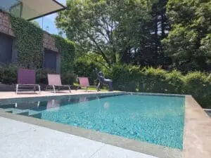 Piscine à débordement en béton brut avec plage en bois exotique et plantations modernes à Thonon-les-Bains, réalisée par Pernollet Paysage
