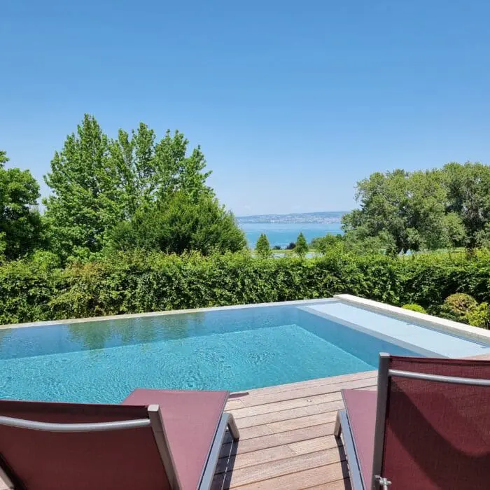 Piscine à débordement en béton brut avec plage en bois exotique et volet immergé à Thonon-les-Bains, réalisée par Pernollet Paysage