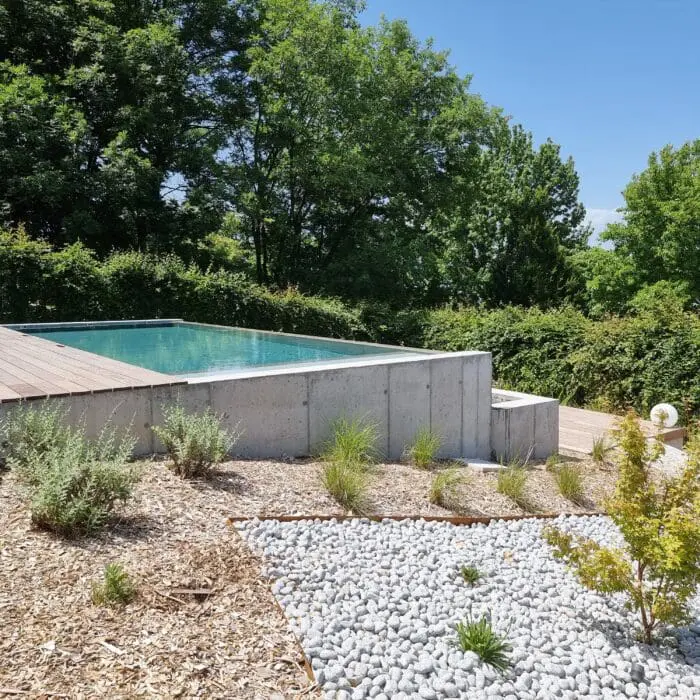 Piscine à débordement avec plage en bois exotique et vue dégagée sur un jardin paysager à Thonon-les-Bains, réalisée par Pernollet Paysage