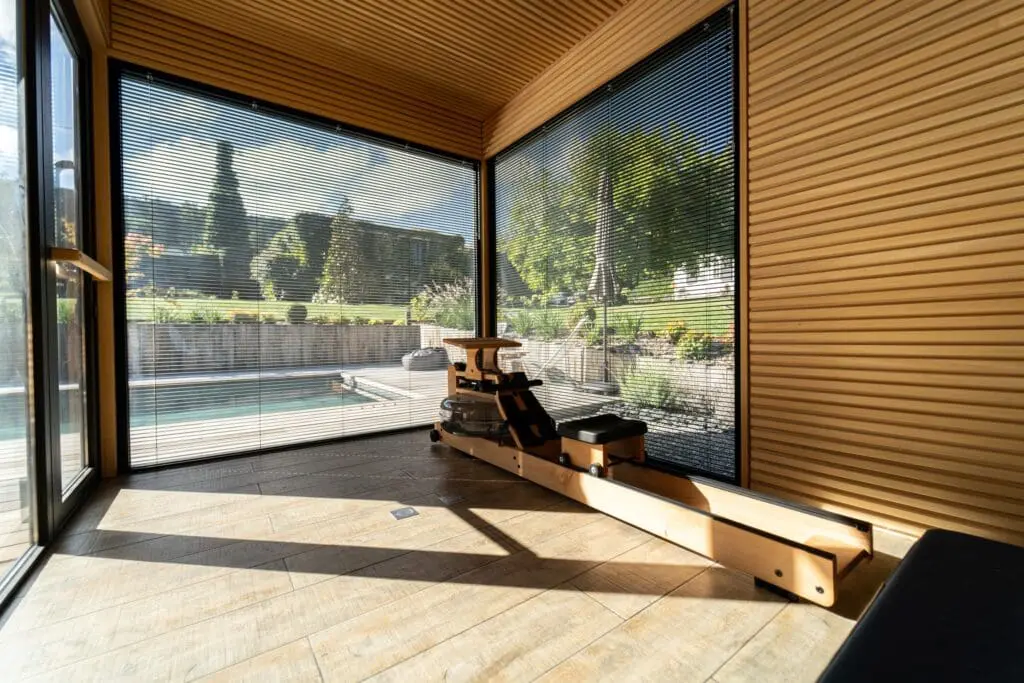 Salle de sport lumineuse avec baie vitrée donnant sur une piscine et un jardin, intégrée dans un espace wellness à Neuvecelle, réalisée par Pernollet Paysage.