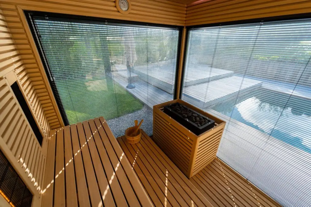 Sauna en bois exotique avec double baie vitrée offrant une vue sur le jardin et une piscine, réalisé par Pernollet Paysage à Neuvecelle.