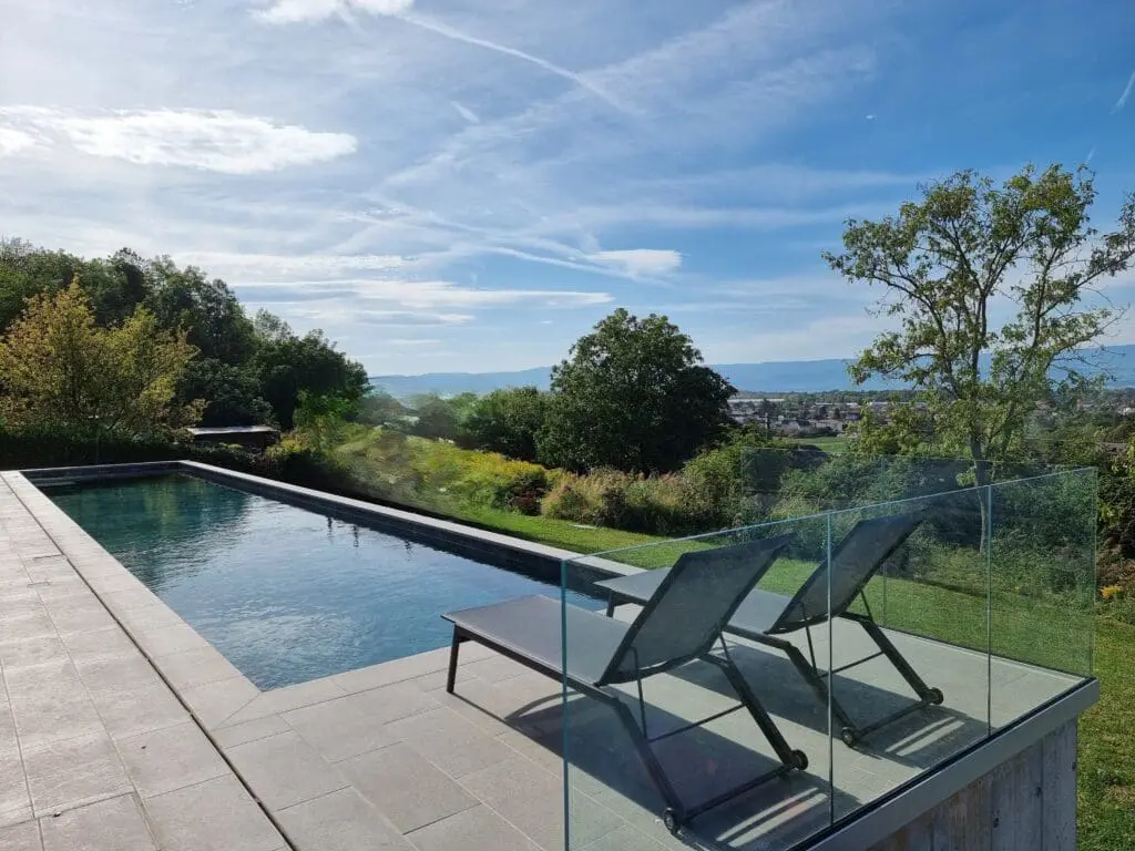 Piscine haut de gamme avec terrasse en grès céram et garde-corps en verre offrant vue sur le lac Léman à Publier.