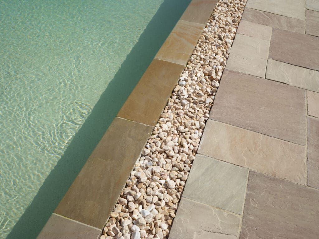 Détail d'une piscine miroir avec margelle en pierre naturelle et drainage en galets à Ballaison en Haute-Savoie (74)