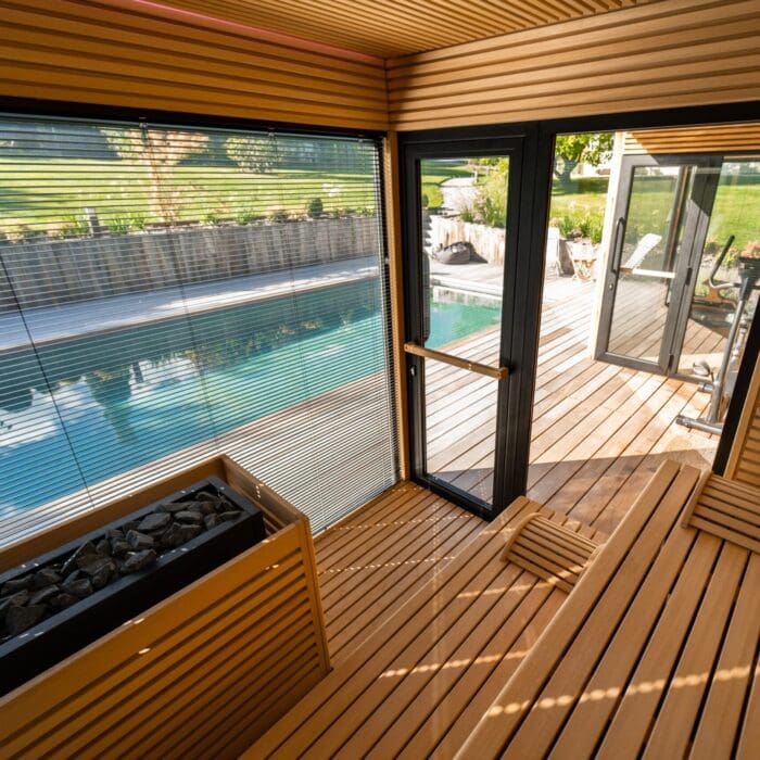 Vue intérieure d’un sauna en bois exotique avec grande baie vitrée donnant sur une terrasse et une piscine, conçu par Pernollet Paysage à Neuvecelle.