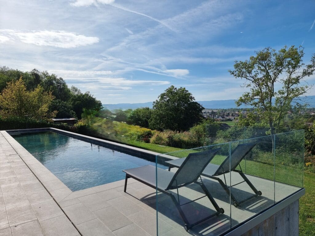 Piscine haut de gamme avec terrasse en grès céram et garde-corps en verre offrant vue sur le lac Léman à Publier.