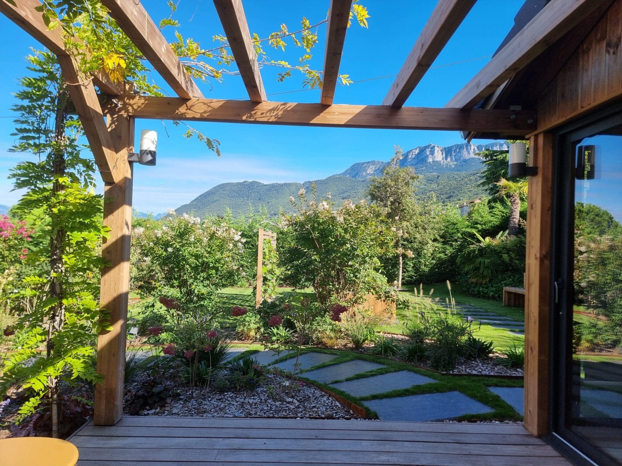 Vue sur le jardin depuis une terrasse en bois sous pergola